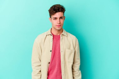 Kafkasyalı genç adam mavi arka planda izole edilmiş üzgün, ciddi yüzlü, mutsuz ve hoşnutsuz..