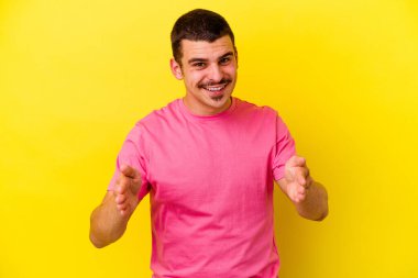 Sarı arka planda izole genç beyaz adam iki eliyle bir şey tutuyor, ürün sunumu.