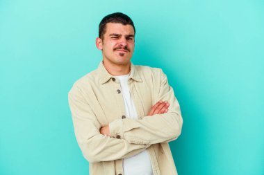 Mavi arka planda izole edilmiş genç beyaz adam alaycı bir ifadeyle kameraya bakarken mutsuz oluyor..