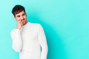 Mavi arka planda izole edilmiş genç beyaz adam rahatlamış bir şeyin fotokopi odasına baktığını düşünüyor..