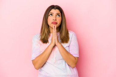 Pembe arka planda izole edilmiş genç Hintli bir kadın. El ele tutuşup, ağzının kenarında dua ediyor..