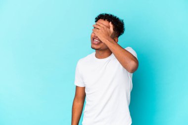 Genç Afro-Amerikan kıvırcık adamı mavi üzerine izole edilmiş gözleri kapamış, gülümseyerek büyük bir sürpriz bekliyor..