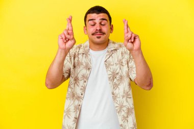 Sarı arka planda izole genç beyaz adam şans dilemek için parmaklarını çapraz