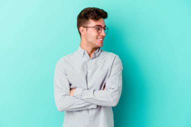 Kafkasyalı genç adam mavi arka planda izole edilmiş gülüyor ve eğleniyor..