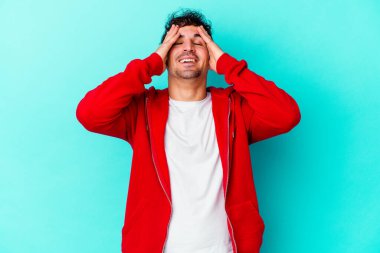 Mavi arka planda izole edilmiş genç beyaz adam ellerini başının üstünde tutarak neşe içinde gülüyor. Mutluluk kavramı.