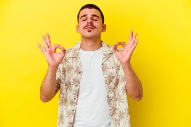 Beyaz tenli genç adam sarı arka planda izole edilmiş sıkı çalışma gününden sonra rahatlıyor, yoga yapıyor..