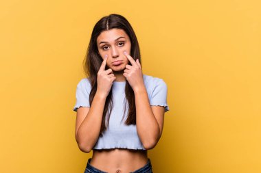 Sarı arka planda izole edilmiş genç bir Hintli kadın ağlıyor. Acı ve kafa karışıklığı gibi bir şeyden mutsuz..