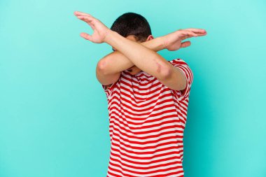 Kafkasyalı genç adam mavi arka planda izole edilmiş iki kolu çapraz tutuyor, inkar kavramı.