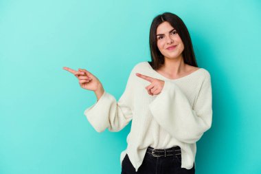 Mavi arka planda izole edilmiş genç beyaz kadın işaret parmaklarıyla fotokopi alanını işaret ederek heyecan ve arzusunu ifade ediyor..