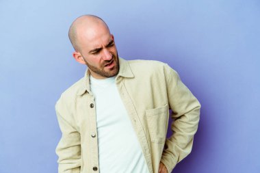 Mor arka planda izole edilmiş beyaz, kel bir adam sırt ağrısı çekiyor..