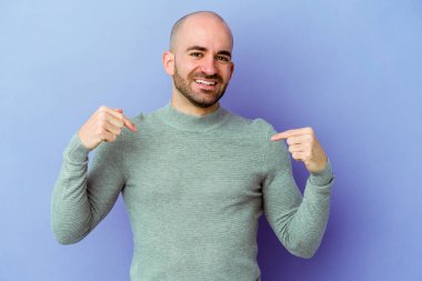 Mor arka planda izole genç beyaz adam parmaklarıyla aşağı noktalar, olumlu duygu.