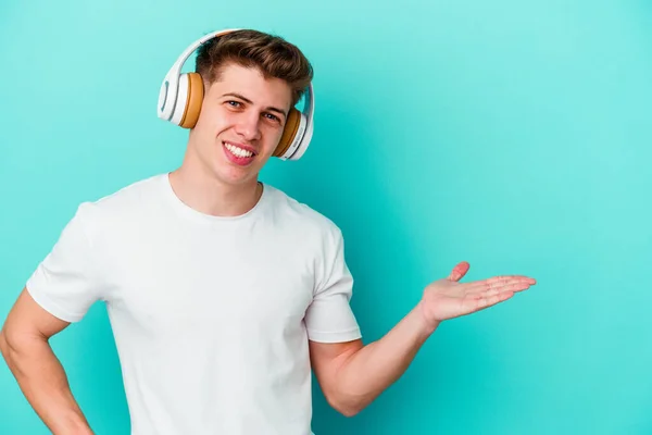 Mladý Kavkazský Muž Poslouchající Hudbu Sluchátky Izolovanými Modrém Pozadí Ukazující — Stock fotografie