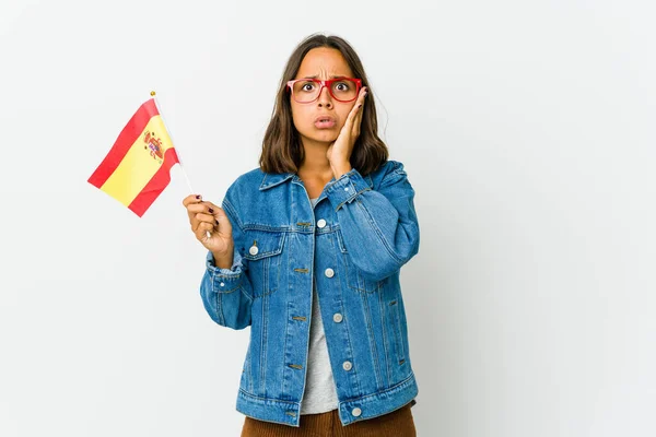 Young spanish woman holding a flag isolated on white background blows cheeks, has tired expression. Facial expression concept.