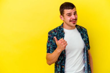 Sarı arka planda izole edilmiş genç beyaz adam işaret parmağıyla fotokopi alanını işaret ederek şok oldu..