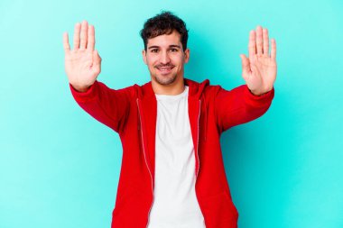 Mavi arka planda izole edilmiş genç beyaz adam on numarayı elleriyle gösteriyor..