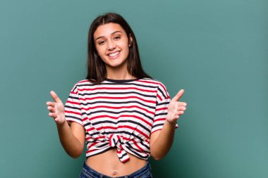 Mavi arka planda izole edilmiş genç Hintli kadın iki eliyle bir şey tutuyor, ürün sunumu..