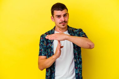 Sarı arka planda izole genç beyaz adam bir mola jesti gösteriyor.