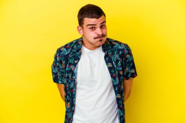 Sarı arka planda izole genç beyaz adam omuzlarını silker ve gözleri açık kalır..