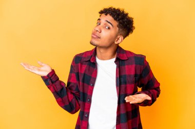 Genç Afro-Amerikalı kıvırcık adam, mor renkte izole edilmiş, kafası karışmış ve omuz silkmiş, bir kopya alanı tutmak için omuz silkiyor..