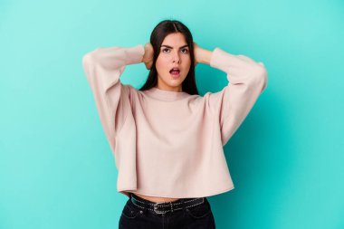 Kafkasyalı genç bir kadın mavi arka planda izole edilmiş kulakları kulaklarıyla kapatıyor çok fazla ses duymamaya çalışıyor..