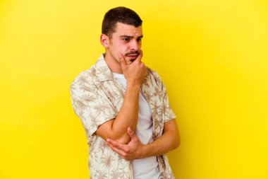 Beyaz tenli genç adam sarı arka planda izole edilmiş şüpheli, belirsiz, seni muayene ediyor..