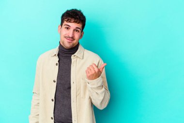 Mavi arka planda izole edilmiş genç beyaz adam işaret parmağıyla fotokopi alanını işaret ederek şok oldu..