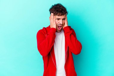 Kafkasyalı genç adam mavi arka planda izole edilmiş kulakları kulaklarıyla kapatıyor çok fazla ses duymamaya çalışıyor..