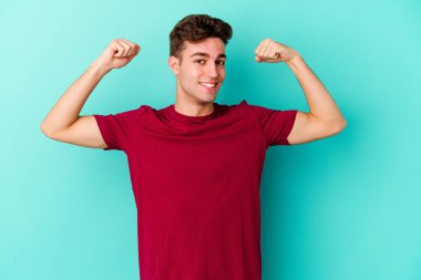 Mavi arka planda izole edilmiş genç beyaz adam güçlü bir hareket sergiliyor kollarıyla, kadınsı gücün sembolü.