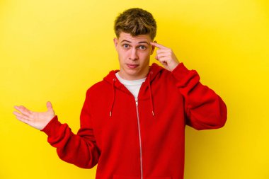 Genç beyaz adam sarı arka planda izole edilmiş ve elinde bir ürün var..