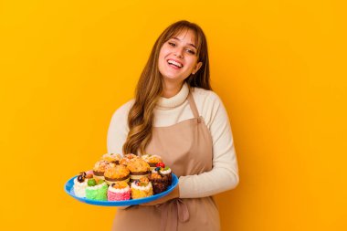 Sarı arka planda izole edilmiş genç pasta şefi kadın gülüyor ve eğleniyor..
