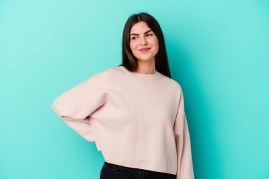 Mavi arka planda izole edilmiş genç beyaz kadın hedeflerine ve amaçlarına ulaşma hayali kuruyor.