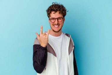 Mavi arka planda izole edilmiş gözlüklü genç beyaz adam parmaklarıyla taş hareketi gösteriyor.