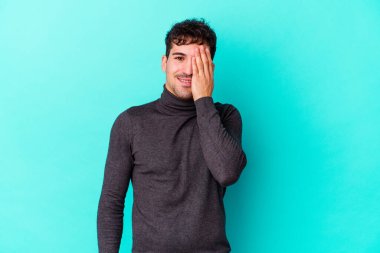 Mavi arka planda izole edilmiş genç beyaz adam yüzünün yarısını palmiye ile kaplayarak eğleniyor..