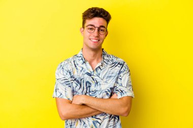 Sarı arka planda izole edilmiş genç beyaz adam kendini güvende hissediyor, kararlılıkla kollarını kavuşturuyor..