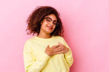 Pembe arka planda izole edilmiş genç Afro-Amerikalı bir kadın, dostane bir ifadeye sahip, avuçlarını göğsüne bastırıyor. Aşk konsepti.