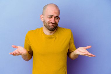 Genç, beyaz, kel bir adam mor arka planda izole edilmiş. Sorgulama sırasında omuz silkiyor ve şüphe duyuyor..