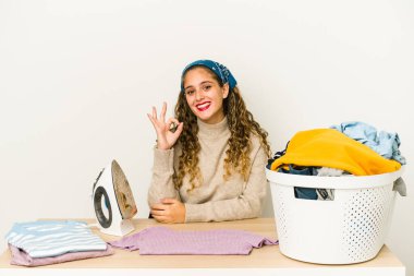 Giysileri ütüleyen beyaz bir kadın neşeli ve kendinden emin..