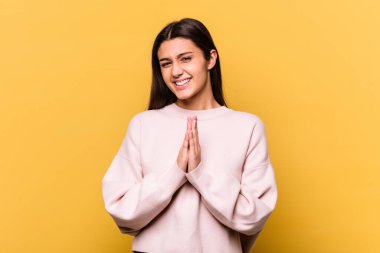 Sarı arka planda izole edilmiş genç bir Hintli kadın el ele tutuşup dua ediyor, kendine güveniyor..