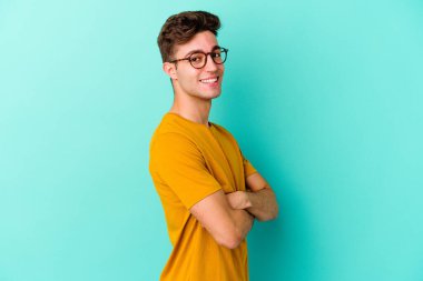 Mavi arka planda izole edilmiş genç beyaz adam mutlu, güler yüzlü ve neşeli.