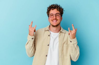 Mavi arka planda gözlük takan genç beyaz bir adam devrim konsepti olarak boynuzlarını gösteriyor..