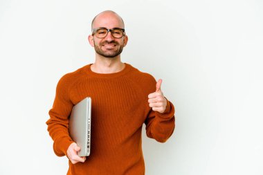 Beyaz arka planda dizüstü bilgisayar tutan genç kel adam gülümsüyor ve başparmağını kaldırıyor.