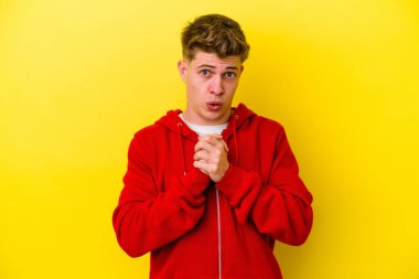 Kafkasyalı genç adam sarı arka planda izole edilmiş şans için dua ediyor, şaşırmış ve ağzını açıp önüne bakıyor..