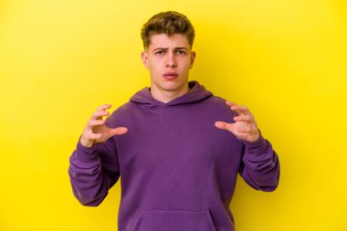 Sarı arka planda izole edilmiş genç beyaz bir adam elinde avuç içi bir şeyle kameraya sunuyor..