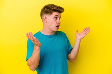 Sarı arka planda izole edilmiş genç beyaz adam gökyüzüne haykırıyor, yukarı bakıyor, hayal kırıklığına uğramış..