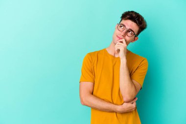 Mavi arka planda izole edilmiş genç beyaz adam rahatlamış bir şeyin fotokopi odasına baktığını düşünüyor..