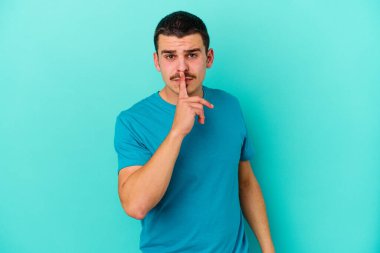 Mavi arka planda izole edilmiş genç beyaz bir adam ya sır saklıyor ya da sessizlik istiyor..