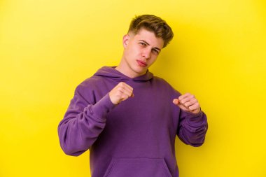Sarı arka planda izole edilmiş genç beyaz bir adam bir tartışma yüzünden yumruk atıyor, öfkeleniyor, kavga ediyor, boks yapıyor.