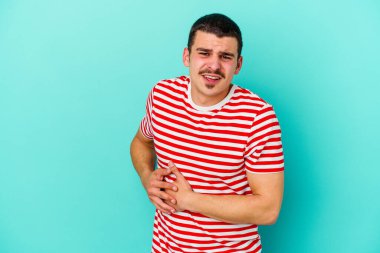 Mavi arka planda karaciğer ağrısı çeken, karnı ağrıyan genç beyaz bir adam..