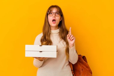 İzole edilmiş arka planda pizza tutan beyaz bir kadın ağzı açık bir şekilde üst tarafı işaret ediyor..