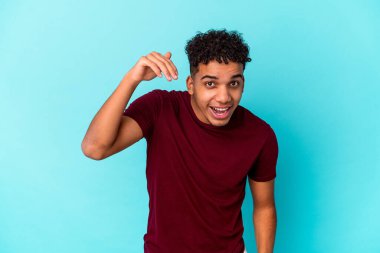 Genç Afro-Amerikalı kıvırcık adam mavi üzerine izole edilmiş bir şekilde bir şeye gülüyor, elleriyle ağzını kapatıyor..